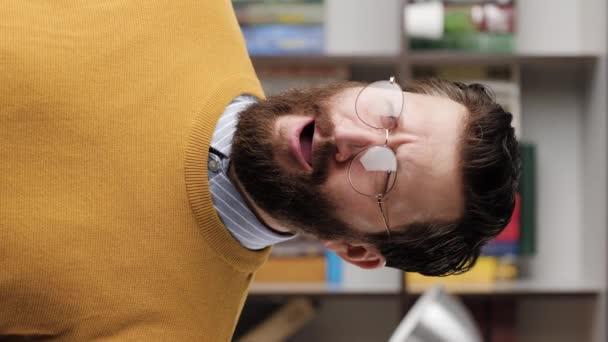 L'homme bâille. vidéo verticale de fatigué homme barbu triste dans des lunettes dans le bureau ou salle d'appartement bâille depuis longtemps, il s'ennuie ou veut dormir. gros plan et ralenti — Video