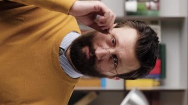 Skepticism, sarcasm emotion. Vertical video of bearded man in glasses in office or apartment room looking at camera and expressing his skeptical attitude and discontent with his look. Close-up