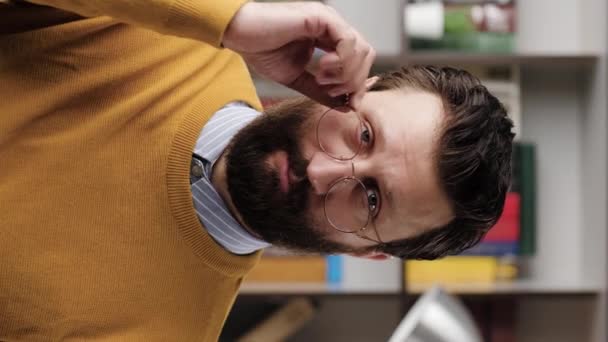 Skepticism, sarcasm emotion. Vertical video of bearded man in glasses in office or apartment room looking at camera and expressing his skeptical attitude and discontent with his look. Close-up — Wideo stockowe