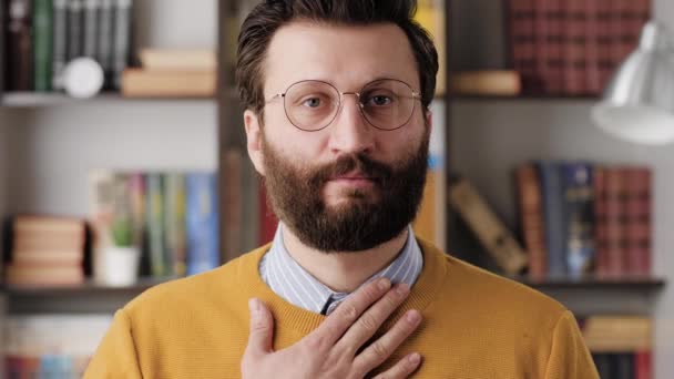 Respect bow. Bearded man with glasses in office or apartment room looking at camera and puts his hand on his chest and bows, expressing respect or greeting. Close-up and slow motion — Stock video