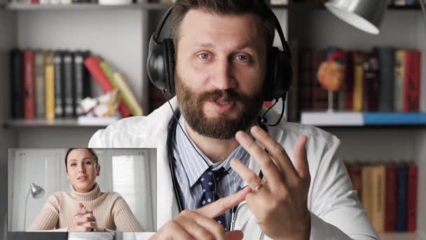 Online therapy, remote patient treatment concepts. Woman patient talking and listens intently on computer webcam with bearded man doctor in headphones on internet video call — Video Stock