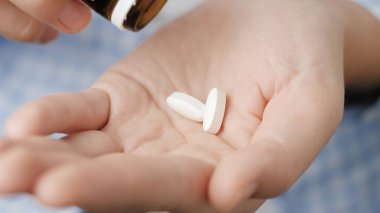 Taking pills. Two big white pills oval diamond-shaped elongated shapes fall into palm of hand from pill bottle. Close-up, front view, center composition
