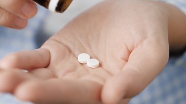 Taking pills. Two average size white round pills fall into palm of hand from pill bottle. Close-up, front view, center composition