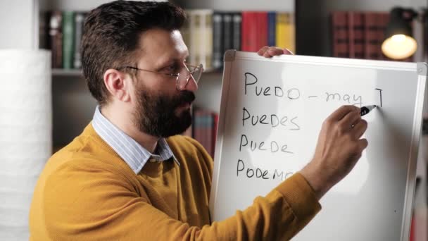 Profesor de español masculino o profesor de inglés hispano hablando y mirando a la cámara y escribiendo palabras en español en el marcador magnético. Traducción de palabras escritas es mayo yo, usted puede, mayo, nosotros podemos — Vídeos de Stock