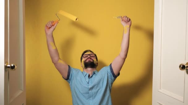 壁の絵画 部屋の改装 作業完了 黄色のペンキで汚れた疲れた男は 新しく塗装された壁の背景に疲れ床に落ちる スローモーション — ストック動画