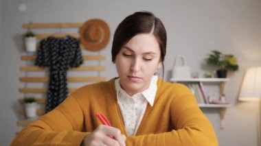 İnternetten öğrenme, video konferans konsepti. Genç bir kadın bilgisayar kamerasının önünde oturmuş konuşuyor ve yazılı notlar alıyor, kameraya bakıyor ve internet sohbetini sürdürüyor.