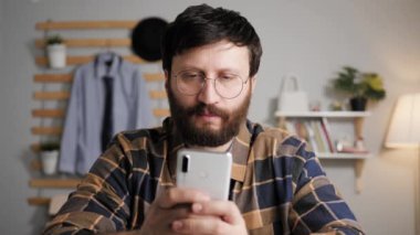 Çevrimiçi öğrenme, video arama konsepti. Gözlüklü bir adam bilgisayar kamerasının önünde oturur, konuşur ve telefonuna notlar alır, kameraya bakar ve internet sohbetini sürdürür.