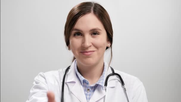 Doctor pulgar hacia arriba. La doctora sonriente positiva sobre fondo gris mirando la cámara levanta la mano y muestra el pulgar hacia arriba. Movimiento lento — Vídeos de Stock