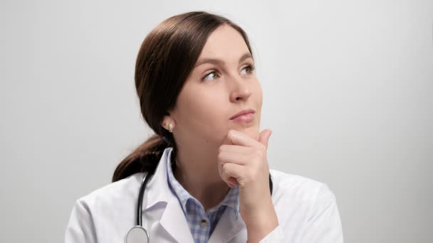 Pensive doctor, brainstorming, good idea concept. Concentrated woman doctor on gray background pensively holds her chin with her hand, inspiration comes and she with smile looking at camera — Stock Video