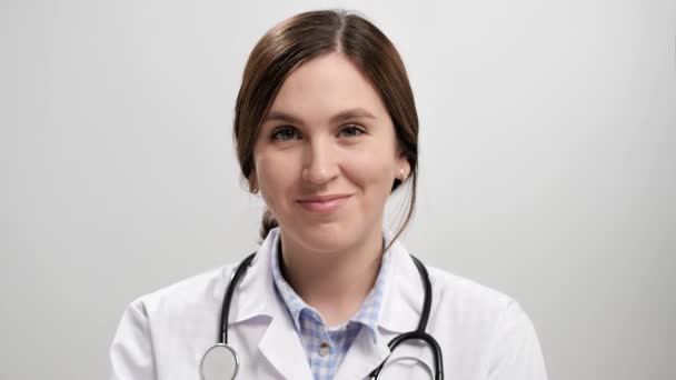 Um gesto de acenar com os dedos. Feliz sorrindo positivo médico mulher em fundo cinza olhando para a câmera e aponta com o dedo e convidar gesto pede para vir a ela. Movimento lento — Vídeo de Stock