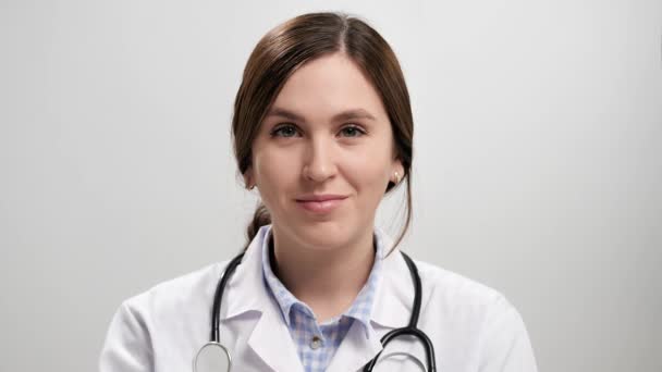 Doctor winks. Positive smiling woman doctor on gray background looking at camera and playfully winking with her right eye. Slow motion — Stock Video