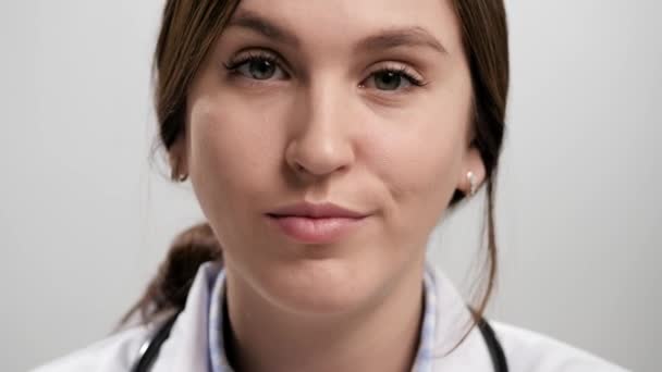 医者の不満問題恥。灰色の背景に不満を持つ女医が目をズレてカメラを見ている。スローモーション — ストック動画