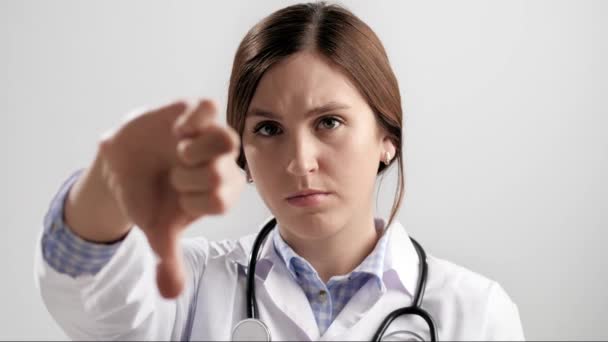 放下大拇指医生严肃的女医生皱着眉头，灰色背景，看着相机，把她的大拇指朝下看。慢动作 — 图库视频影像