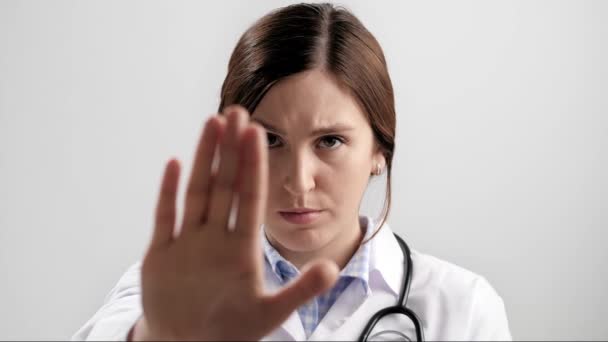 Doctor palm STOP. Fruncir el ceño médico serio mujer sobre fondo gris mirando a la cámara levanta la mano y muestra su señalización de la palma DETENER. Movimiento lento — Vídeos de Stock