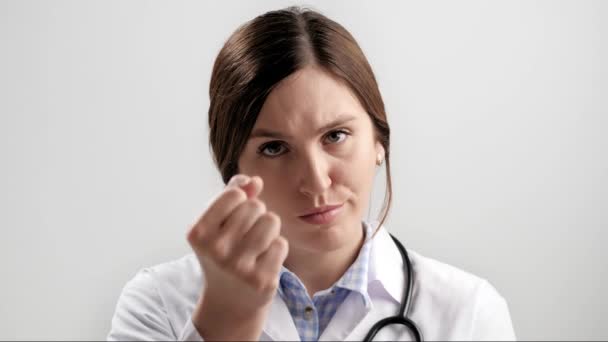 Doutor ameaça a emoção. Médica mulher confiante em fundo cinza olhando para a câmera e mulher ameaça com punho. Movimento lento — Vídeo de Stock