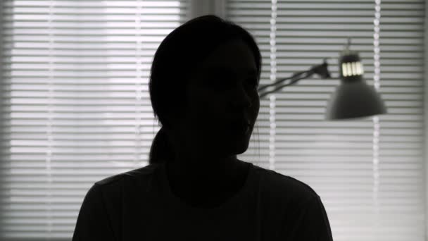 Identité cachée, personne inconnue, silhouette, interview. Silhouette féminine sombre sur fond de lumière de fenêtre parlant en regardant la caméra — Video