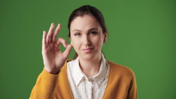 La mujer está bien. Mujer sonriente positiva sobre fondo de croma mirando a la cámara y con gesto su mano derecha mostrando signo OK. Movimiento lento — Vídeos de Stock