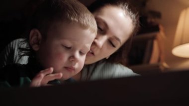 Bebek ve anne telefon ekranını dinliyorlar. Masada oturan ve akıllı telefonla oynayan anne ve çocuğun alt görünümü, ekranda bebek tıklamaları, telefonun kendisi karede görünmüyor. Yakın plan.