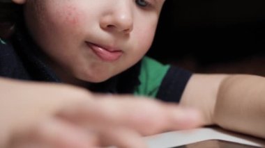 Bebek telefonla oynuyor. Akıllı telefonuyla dikkatle oynayan ve ekranı parmaklarıyla dinleyen çocuğun yüzüne yakın plan çekimde, kamera sırayla yüzünü ve ellerini gösteriyor. Yavaş çekim