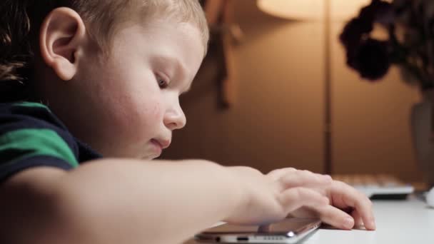 Baby spielt mit Telefon. Nettes Kind sitzt am Tisch und konzentriert sich auf den Bildschirm des Smartphones, das sich unkontrolliert auf dem Tisch dreht. Nahaufnahme und Zeitlupe — Stockvideo