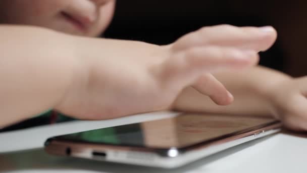 Kind spielt mit Handy. Großaufnahme von Kinderhänden auf dem Bildschirm des Smartphones, das auf einem weißen Tisch liegt. Zeitlupe — Stockvideo