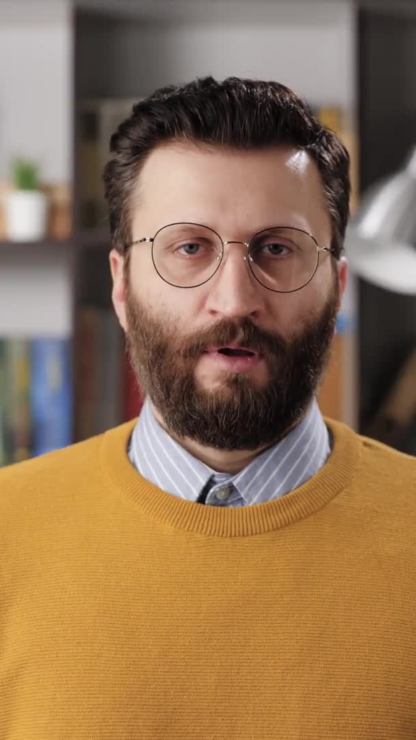 Toc toc, ¿hay alguien en casa? Vídeo vertical de un hombre de barba escéptico profesor o empresario con gafas mirando a la cámara y golpeando a la cámara. Movimiento lento — Vídeos de Stock