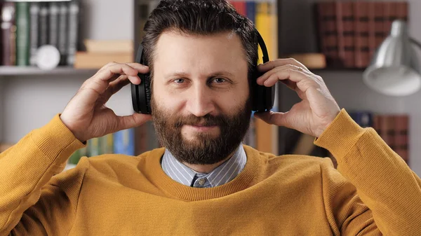 Online learning, remote education, video call, e-learning, remote presentation concept. Positive bearded man looking at camera hold wireless headphones with his hands. Medium shot