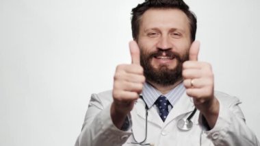 Doktor parmak yukarı. Beyaz arka planda gülümseyen ve gülen bir adamın portresi kameraya bakıyor ve başparmağını iki eliyle gösteriyor.