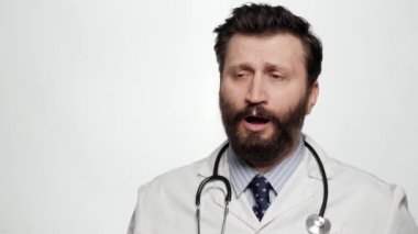 Doktor esniyor. Beyaz arka plandaki yorgun doktor portresi esniyor ve ağzını eliyle kapatıyor.