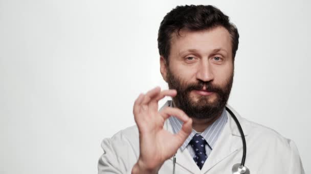 Doctor OK. Retrato de hombre sonriente positivo médico sobre fondo blanco mirando a la cámara y muestra gesto OK con los dedos — Vídeo de stock