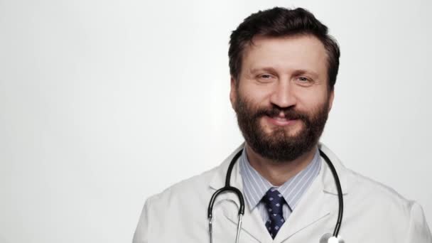 Doctor HELLO. Sonriente positivo hombre risueño médico sobre fondo blanco mirando a la cámara y saludando con la mano derecha mostrando y dice hola — Vídeos de Stock