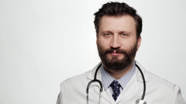 Doktor göz kırpıyor. Beyaz arka planda gülümseyen bir adamın portresi kameraya bakıyor ve göz kırpıyor. — Stok video