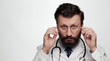 Doktor şaşırdı, şok oldu. Beyaz arka plandaki kafası karışmış doktor şaşırmış yüzüyle gözlüğünü çıkarıp kameraya bakıyor.