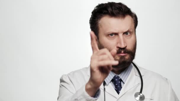Доктор угрожает пальцем. Серьёзный хмурый доктор на белом фоне смотрит в камеру и угрожающе указывает указательным пальцем. — стоковое видео