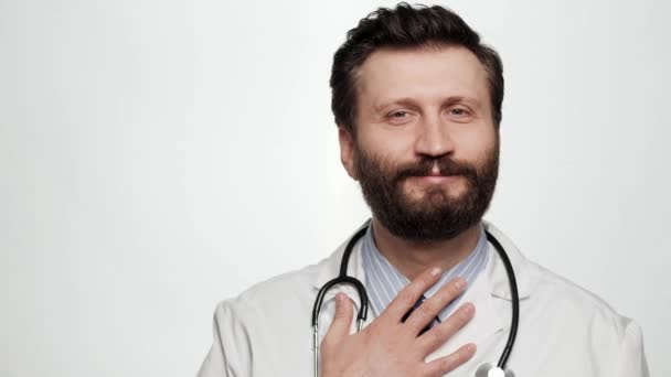 Medico rispetto arco. Sorridente uomo medico su sfondo bianco guardando la fotocamera e mette la mano sul petto e archi, esprimendo rispetto o saluto — Video Stock