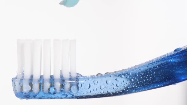 Kartáček na zuby a zubní pastu. Makro pohled na modrý zubní kartáček, na kterém je modrá zubní pasta vymačkána na bílém pozadí. Zpomalený pohyb — Stock video