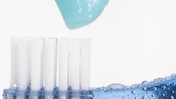 歯ブラシと歯磨き粉。青の歯ブラシでゆっくりと白い背景に青の歯磨き粉を圧迫。マクロビューとスローモーション — ストック動画