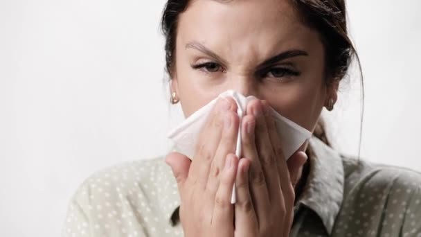 Congestion nasale, écoulement nasal. Femme avec des symptômes de rhume et de grippe sur fond blanc souffle son nez dans une serviette en papier. Gros plan et ralenti — Video