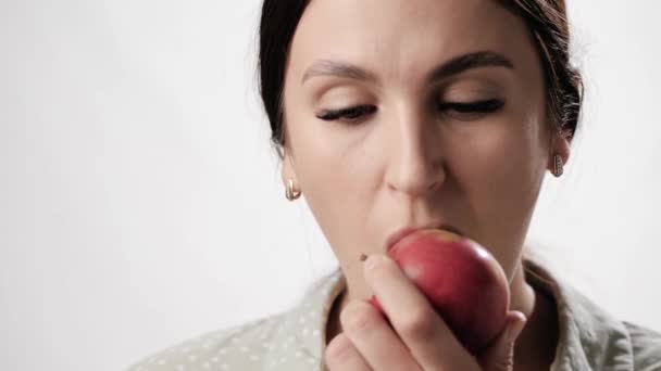 A nő almát eszik. Boldog mosolygós nő fehér háttér harap le egy darab almát, és rágja meg örömmel. Közelkép és lassított felvétel — Stock videók