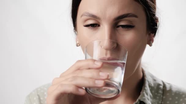 Gevoelige tanden. Vrouw op witte achtergrond drinkt water uit glas en heeft kiespijn als gevolg van gevoeligheid van haar tanden. Close-up en slow motion — Stockvideo