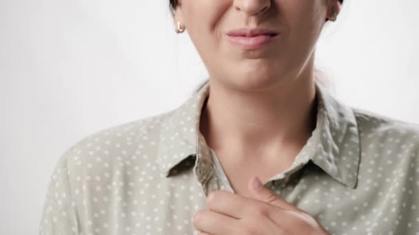 Αναπνευστικά προβλήματα, πόνος στο στήθος. Μια γυναίκα που υποφέρει σε λευκό φόντο αγγίζει το στήθος με το χέρι της. Αργή κίνηση και κοντινό πλάνο — Αρχείο Βίντεο