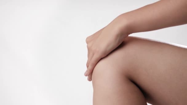 Dor ou alívio da dor no joelho. A mão feminina no fundo branco toca suavemente no joelho. Close-up e câmera lenta — Vídeo de Stock