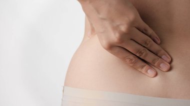 Sırt ağrısı. Kadın eli, beyaz arka planda beline dokunur ve bastırır. Yakın çekim görünümü