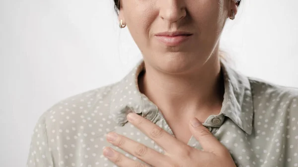 Breathing problems, chest pain. Suffering woman on white background touches chest with her hand. Close-up view