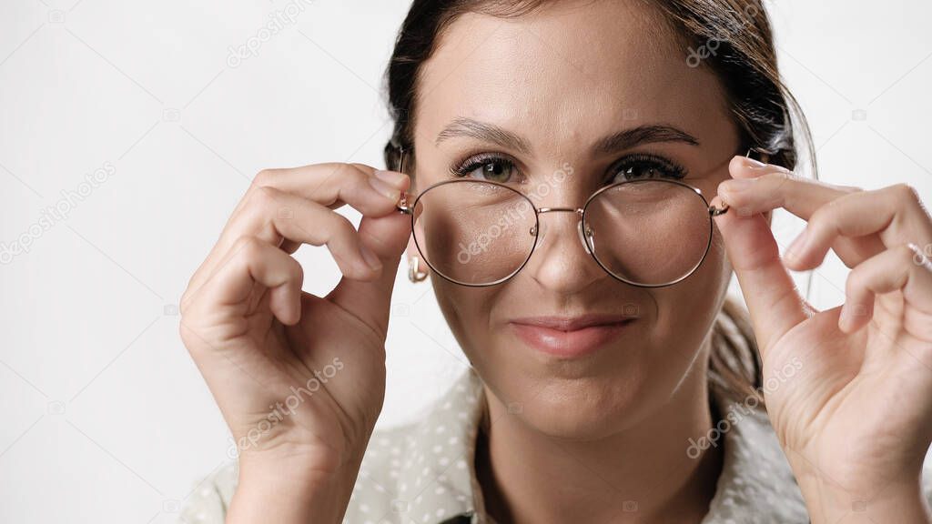 Woman puts on glasses. Smiling positive woman on white background looking at camera and puts on glasses. Vision problems, student, teacher and education concepts