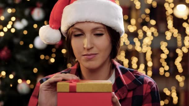 Концепция "С Новым годом и Рождеством". Женщина открывает подарок и смотрит на то, что внутри ослепительно яркий свет светит на ее лицо из коробки, женщина закрывает подарок и смотрит на камеру улыбаясь. Крупный план — стоковое видео