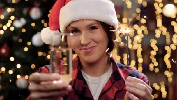 Boldog nő mosolyog és a kamerába néz, csillagszórót és egy pohár pezsgőt tart a kezében, pirítóst gesztikulál és bort iszik. Boldog karácsonyt és boldog új évet! Közelkép — Stock videók