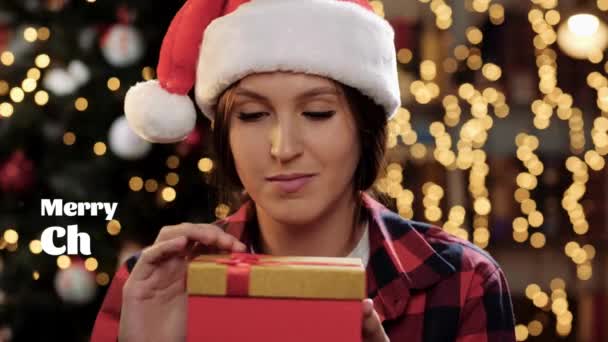 Καλά Χριστούγεννα και ευτυχισμένο το νέο έτος κείμενο. Γυναίκα ανοιχτό δώρο και κοιτάζει τι είναι μέσα, εκθαμβωτικό έντονο φως λάμπει στο πρόσωπό της από το κουτί, γυναίκα κλείνει το δώρο και κοιτάζει κάμερα χαμογελώντας. Κοντινό πλάνο 60 fps — Αρχείο Βίντεο