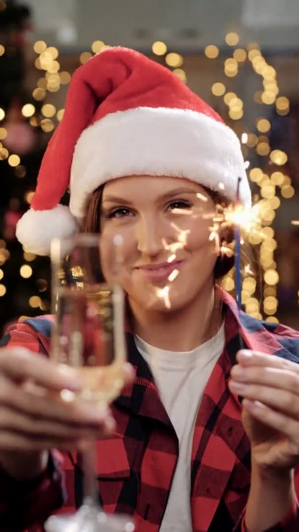 God Jul och Gott nytt år koncept. Vertikal syn på glad kvinna ler och tittar på kameran, hon håller glitter och glas champagne och hon gör rostat bröd gest och dricker vin. Närbild — Stockvideo