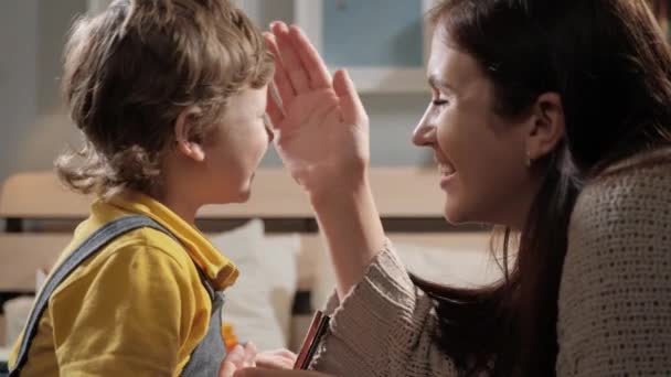 Zärtlichkeit. Mutter und Baby sitzen auf dem Bett im Schlafzimmer und Mutter streicht sanft über das Babygesicht, und dann küsst Mutter Baby. Zeitlupe und Nahaufnahme — Stockvideo